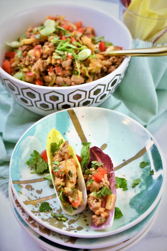 Chinese turkey endive bites on stack of modern green and gold appetizer plates with bowl of turkey with gold spoon in background