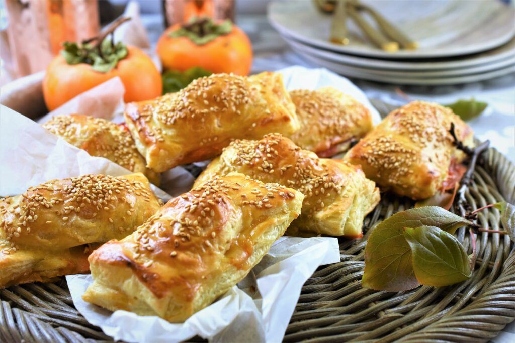 persimmon ham and swiss puff with hot pepper jelly on round wicker tray with fresh Fuyu persimmons in the background