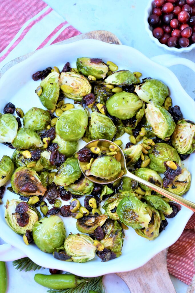 white ceramic round handled side dish with roasted Brussels sprouts with cranberry Serrano vinegar on red and white kitchen towel